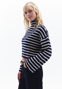 Marinblå och vit randig tröja med hög hals, kort design och vida ärmar, tillverkad av ribbad stickad material.