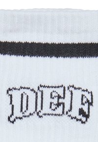 Weißer Socken mit gerippter Textur, der die schwarze Beschriftung "DIES" in einer fetten, stilisierten Schriftart nahe dem Bündchen zeigt. Akzentuiert mit einem schwarzen Streifen.