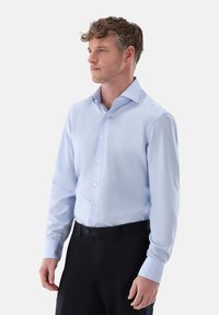 Camicia azzurro chiaro con colletto button-down, maniche lunghe e texture liscia. Indossata con pantaloni scuri, caratterizzati da un design slim fit.