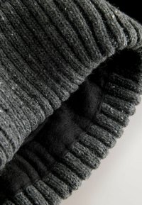 Teren de culoare gri închis, realizat dintr-un material tricotat cu o textură striată, având un interior moale și pufos și detalii de cusătură evidente pe margini.