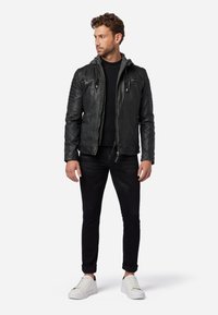 Svart läderjacka med huva, kviltat axeldetalj, långa ärmar, två bröstfickor och en figurnära design. Bärs med svarta jeans och vita sneakers.
