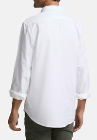 Camisa blanca de manga larga con puños enrollados, cuello abotonado y dobladillo curvado, confeccionada en una tela suave y ligera.