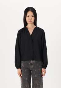 Svart långärmad skjorta med V-hals, knäppning framtill och rynkad detalj vid axlarna. I kombination med jeans med stjärnmönster.