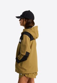 Lysebrun jakke med sorte detaljer, hætte og lommer. Båret med en sort kasket, der viser en afslappet pasform og holdbart stof.