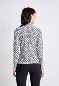 Langärmliges Oberteil in Weiß und Schwarz mit einem geometrischen sechseckigen Muster, das einen hohen Ausschnitt und eine figurnahen Schnitt aufweist.