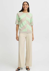 Leichter Pullover in Beige mit mintgrünem Chevron-Muster und kurzen Ärmeln, kombiniert mit cremefarbenen weiten Hosen und schwarzen Sandalen.