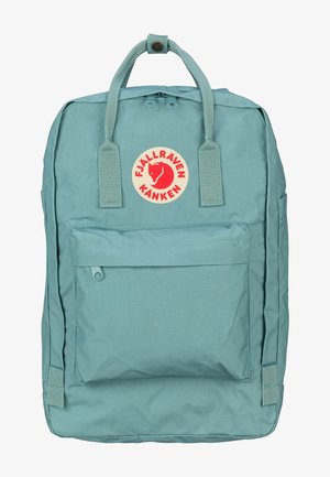 Un sac à dos Fjällräven Kanken bleu clair présente une forme rectangulaire, une poche zippée à l'avant, deux poches latérales et un patch logo circulaire.