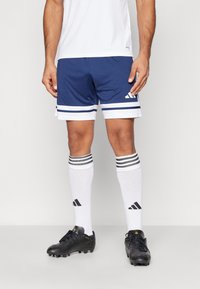 Marina atletiska shorts med vita ränder, i kombination med knähöga vita strumpor med svarta ränder. Svarta fotbollsskor fulländar outfiten.