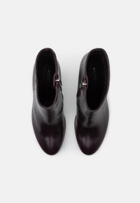 Stivali ankle in pelle bordeaux dalla forma slim, con cerniera laterale e texture liscia. I dettagli cuciti vicino alla cerniera accentuano il design.