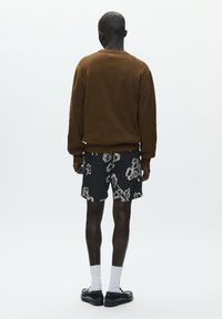 Sweat-shirt marron, short noir à motifs floraux, chaussettes blanches et chaussures noires, vu de dos sur fond blanc.