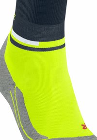 Calzini sportivi con un vivace corpo giallo neon, tallone grigio e parte superiore della caviglia scura. Dotati di strisce decorative nere e bianche.