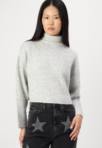 Lys grå ribbestrikket turtleneck-genser med dropped shoulders, parret med høydejusterte svarte jeans som har stjernepynt.
