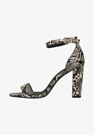 Sandalia de tacón alto para mujer con estampado de piel de serpiente en blanco y negro, con una correa en el tobillo con hebilla cuadrada y tacón ancho.