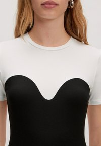 Zwart-wit t-shirt met korte mouwen, ontworpen met een aansluitende pasvorm en een ronde, golvende halslijn. Glad stofoppervlak met contrasterende kleuren.