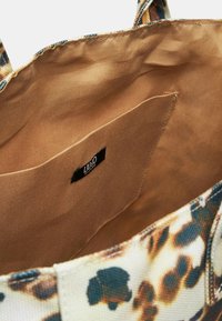 Vista interna di una borsa con una fodera in tessuto beige morbido, dotata di una tasca e un'etichetta con logo nera. L'esterno è decorato con una stampa animale.