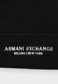 Tessuto nero a maglia con testo ricamato "ARMANI EXCHANGE MILANO / NEW YORK" in bianco. Design semplice, texture liscia.
