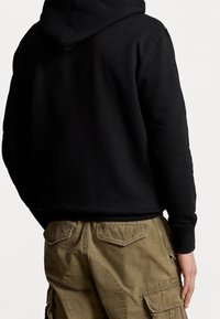 Svart bomullsu hoodie med huva, med en enkel design. Kombinerad med olivgröna cargobyxor med fickor och en strukturerad yta.