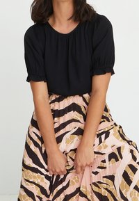 Svart topp med puffärmar och rund halsringning, tillsammans med en veckad kjol med ett mönster i rosa, svart och beige djurmönster.