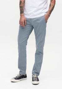 Svijetloplave chinos hlače s teksturiranim materijalom, slim fit kroja, bočnim džepovima i ležernim stilom, uparene s crnim niskim tenisicama.