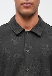 Mørk grå polo skjorte med et strukturert mønster, med krage og tre knapper foran. Mykt stoff med subtile detaljer.