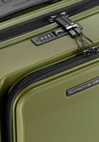 Equipaje rígido de color verde con superficie texturizada, cremalleras negras, un candado de combinación incorporado y un acento de logotipo en negro.