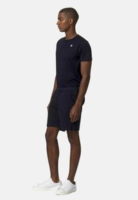 Shorts blu navy e t-shirt coordinata, entrambi in un tessuto morbido e leggero. Sneakers bianche con dettagli perforati completano l'outfit.