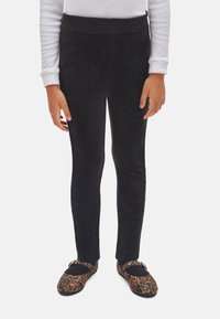 Leggings de pana negra con cinturilla elástica, combinados con zapatos marrones de estampado de leopardo con detalles de hebilla.