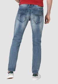 Verblasste blaue Jeans mit slim fit, fünf Taschen und Nähte als Akzent. Getragen mit weißen und grünen Schuhen. Rückansicht.