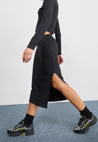 Svart ribbat långkjol med sidssplit, parat med svarta och grå sneakers med gula accenter. Outfitten är figurnära och modern.