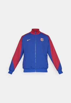 Chaqueta de atletismo de Nike con cuerpo azul, mangas rojas, cuello alto, cremallera frontal y logo de Barcelona en el pecho con detalles en dorado.