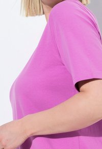 Tričko s krátkým rukávem v živé růžové barvě z bavlněné směsi; hladká textura s uvolněným střihem a kulatým výstřihem; viditelné švy na rukávech.