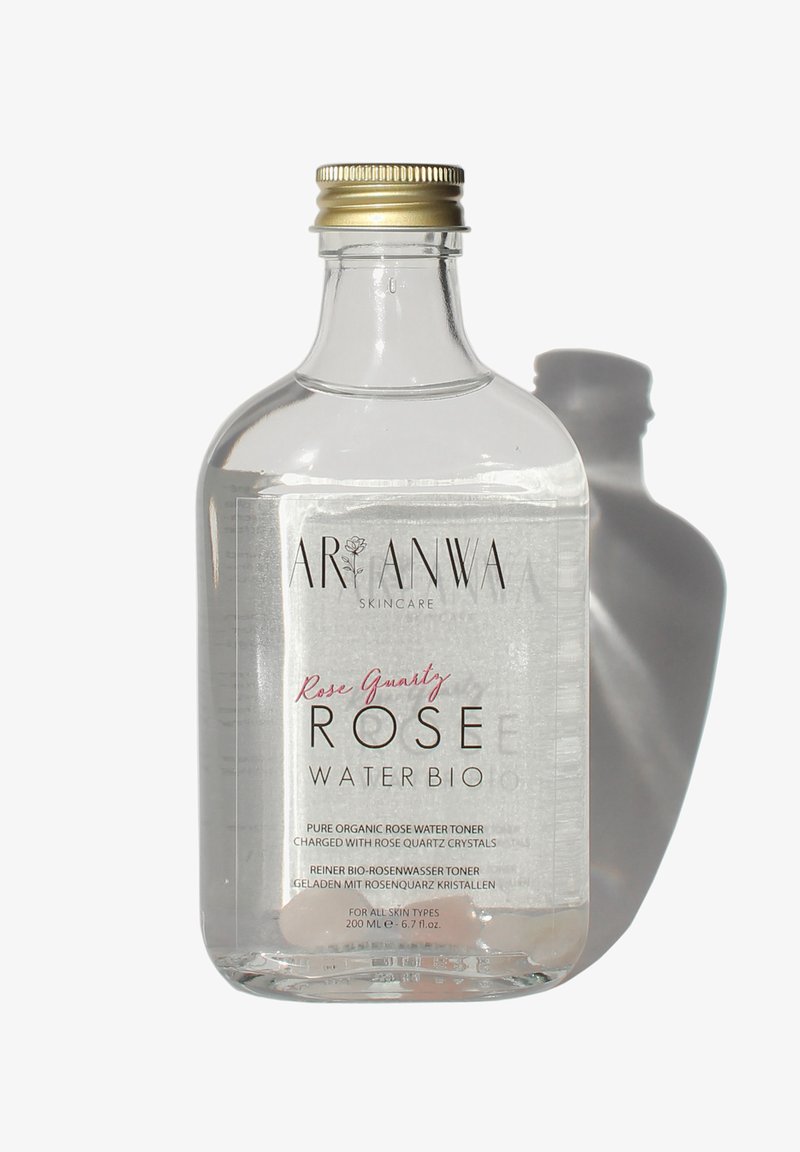 Clear bottle of Aranwa Skincare Rose Quartz Rose Water Bio toner with gold cap and pink crystal at base, casting a shadow.