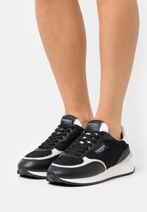 Zwart-witte sneakers met een zwart textiel bovenwerk met textuur, gladde zwarte lederen accenten, een witte zool en een opvallend logo op de tong.