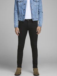 Pantalones vaqueros negros ajustados con una textura suave, combinados con una chaqueta de mezclilla azul clara y una camiseta blanca, acabados con botas de tobillo marrones.