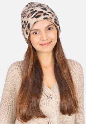 Beige Strickmütze mit einem Leopardenmuster in Braun und Schwarz. Der Stoff wirkt weich und sitzt eng, ergänzt durch einen neutral gefärbten Pullover.