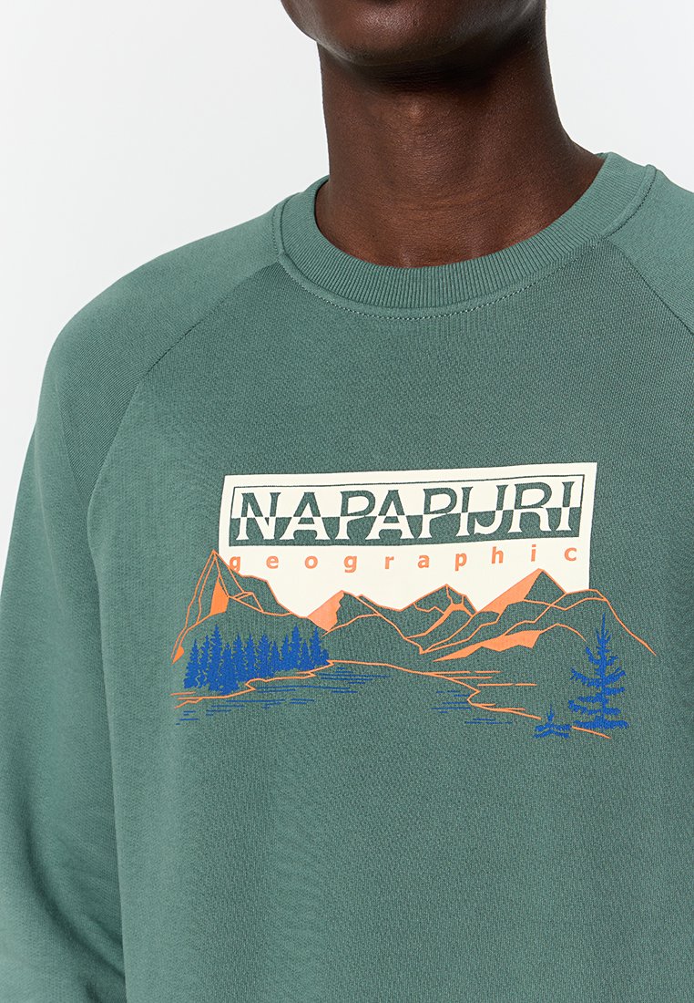 Zielona bluza z okrągłym dekoltem, z nadrukowanym krajobrazem w odcieniach pomarańczowego i niebieskiego. Miękka tkanina z raglanowymi rękawami.
