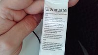 Etichetta di lavaggio su tessuto bianco, con istruzioni per la cura in diverse lingue, comprese le icone per i metodi di lavaggio e asciugatura, tenuta in mano.