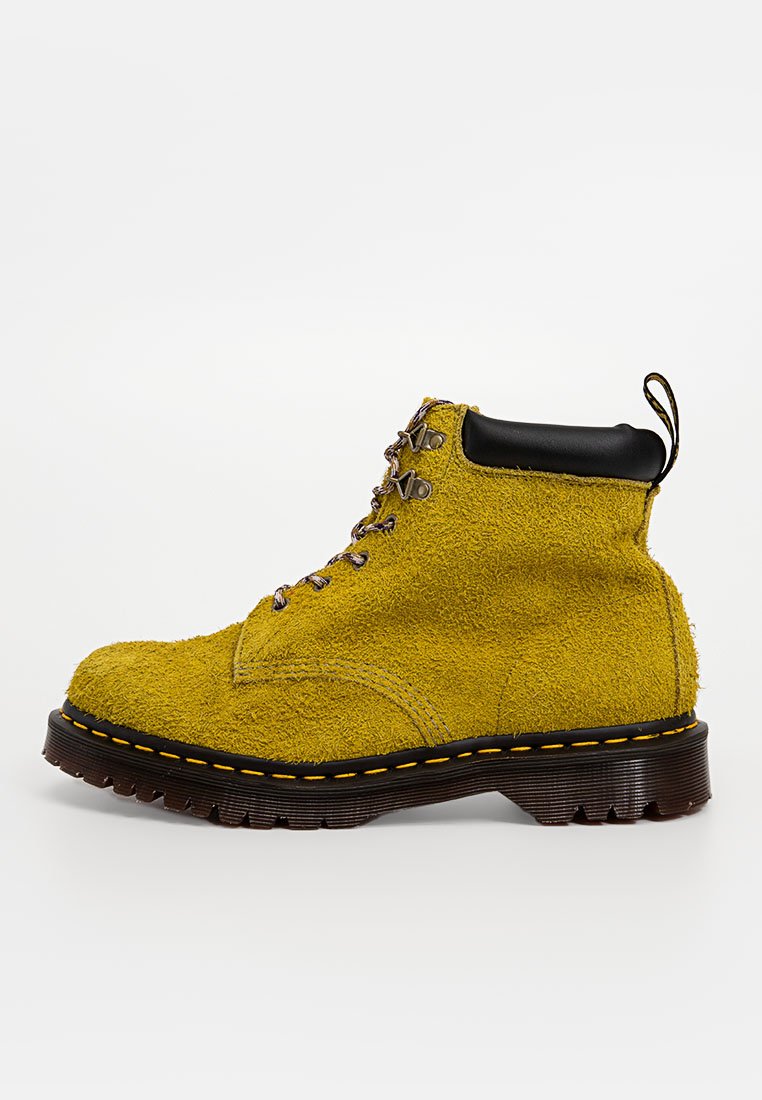 Gelbe Wildleder-Ankle-Boots mit schwarzen Lederakzenten, ausgestattet mit Metall-Ösen und einer dicken, strukturierten Gummisohle mit einem gelben Steppdetail.