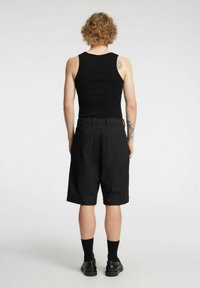 Czarny top na ramiączkach i czarne szorty typu cargo, o luźnym kroju, z dwoma tylnymi kieszeniami i gładką fakturą. Noszone z czarnymi skarpetami i butami.