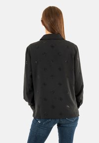 Blusa nera a maniche lunghe con colletto, caratterizzata da un motivo testurizzato di piccoli motivi ricamati lucidi. Tessuto liscio, vestibilità casual.