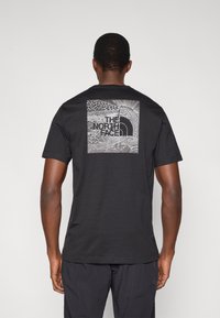 Μαύρο βαμβακερό T-shirt με γραφική εκτύπωση στην πλάτη, που απεικονίζει ένα λεπτομερές μαύρο και λευκό σχέδιο με το λογότυπο "The North Face".