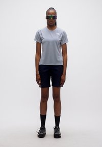 Γυναίκα που στέκεται με τα χέρια δίπλα στο σώμα φορώντας γκρι μπλουζάκι, μαύρο σορτς, μαύρες κάλτσες, παπούτσια πεζοπορίας και αθλητικά γυαλιά ηλίου με αντανάκλαση.