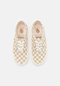 Beige och vita rutiga Vans-sneakers med vita snören, metallöglor och synliga varumärkesetiketter inuti skorna och på sidan.