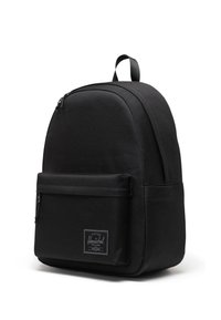 Sac à dos en tissu noir avec une forme arrondie, poche zippée à l'avant et une étiquette logo rectangulaire. Texture lisse et bretelles réglables.