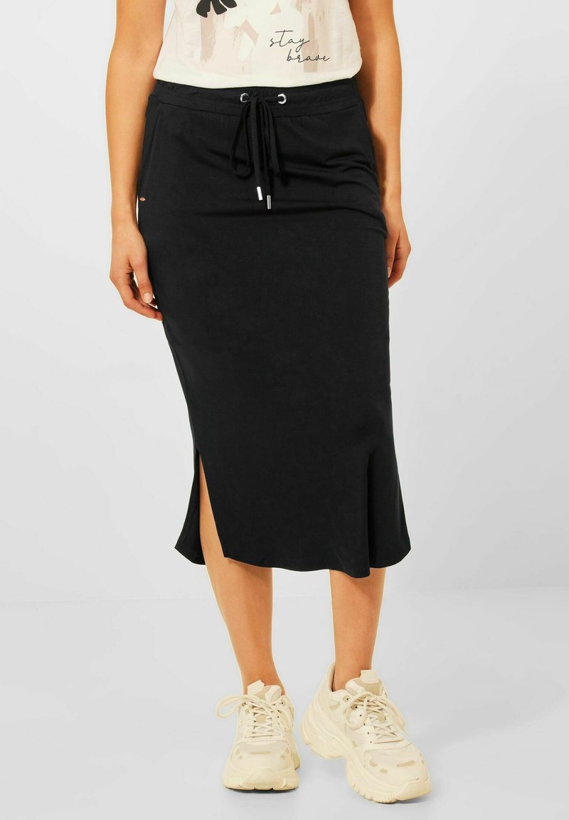 Czarna midi spódnica z regulowanym sznurkiem w talii, bocznym rozcięciem i miękką fakturą, zestawiona z jasnymi trampkami na codzienny, swobodny look.