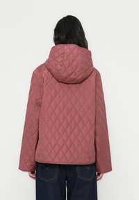 Πουπουλένιο ροζ-κόκκινο μπουφάν με κουκούλα, με τετράγωνο σχήμα και μεγάλα διαμάντια σχέδια. Ομαλή υφή και πλατύτερα μανίκια είναι ορατά.