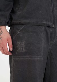 Joggers neri in tessuto testurizzato con logo in rilievo sulla tasca. Presentano una vestibilità rilassata e una vita elasticizzata per il massimo comfort.