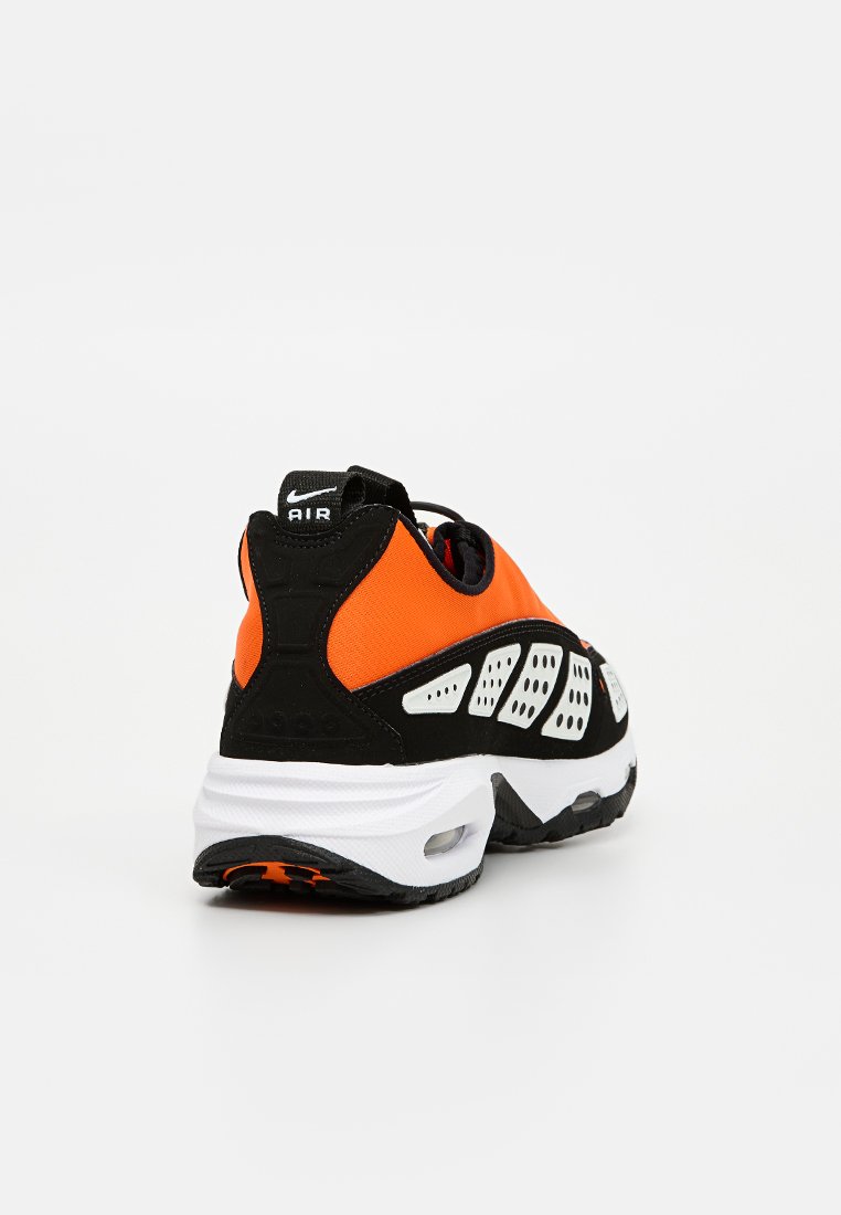 Zapatilla deportiva negra y naranja con parte superior de tela texturizada, suela blanca, perforaciones destacadas y detalle de amortiguación de aire visible.