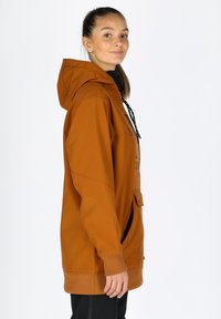 Felpa arancione con cappuccio, dal taglio morbido, tessuto testurizzato, tasca frontale e cordini neri. Il modello si posa di lato, mettendo in risalto il design.