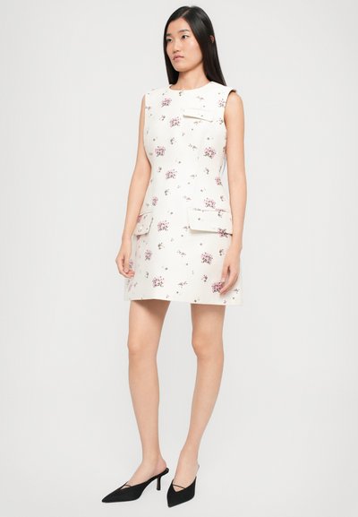 Valge ilma varrukateta kleit väikese lilla lillemustriga, kahe ees oleva taskuga ja sirge lõikega. Kombineeritud mustade terava ninaga kontsakingadega.